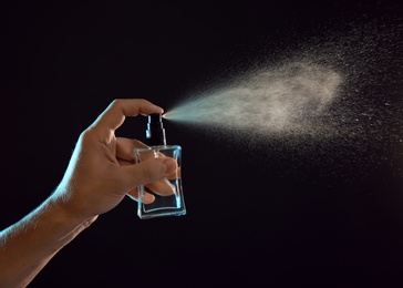 Young man spraying perfume on black background, closeup