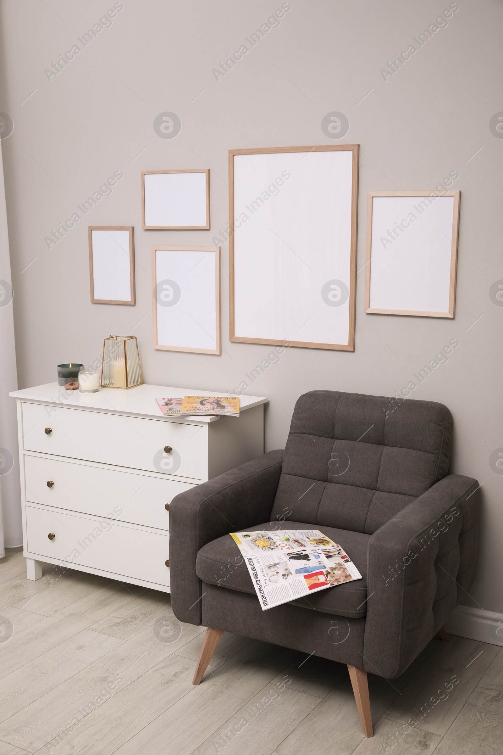 Photo of Empty frames hanging on grey wall over white chest of drawers in room. Mockup for design