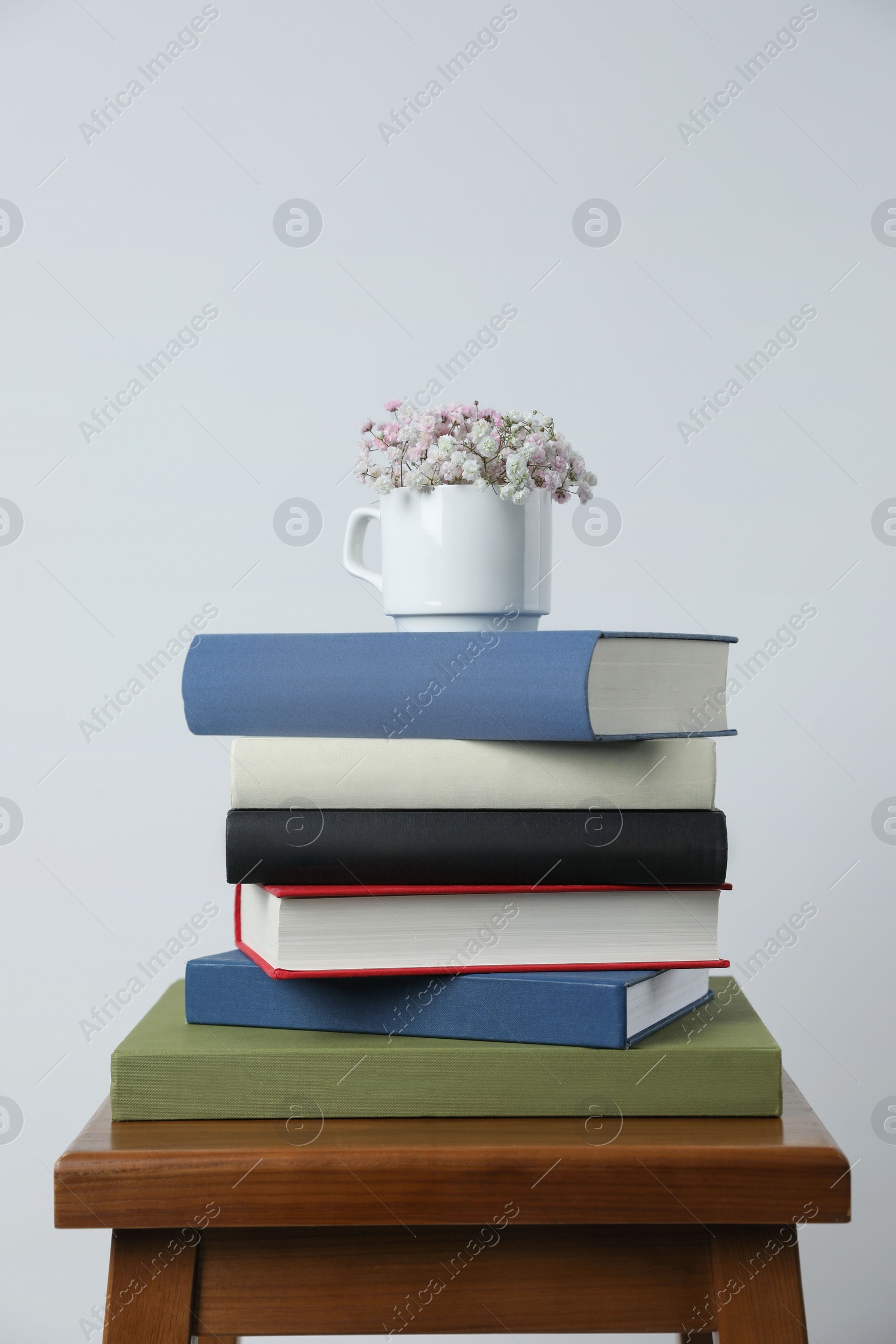 Photo of Hardcover books and cup with flowers on wooden stool near white wall