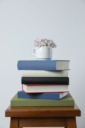 Hardcover books and cup with flowers on wooden stool near white wall