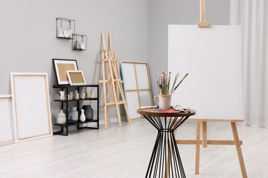 Wooden easel with canvas near paints, palette and brushes in artist's studio, space for text