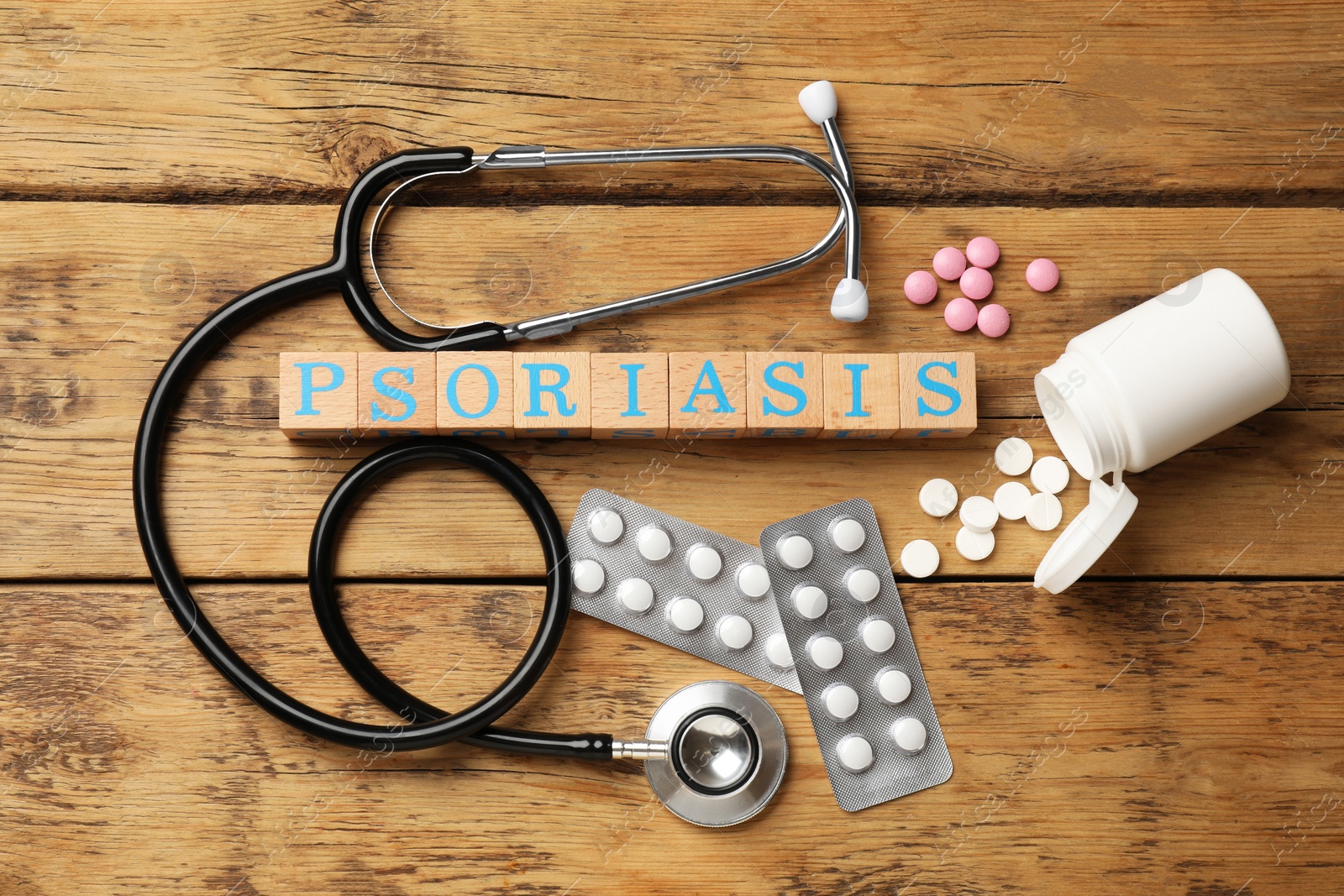 Photo of Word Psoriasis made of cubes with letters, stethoscope and pills on wooden table, flat lay