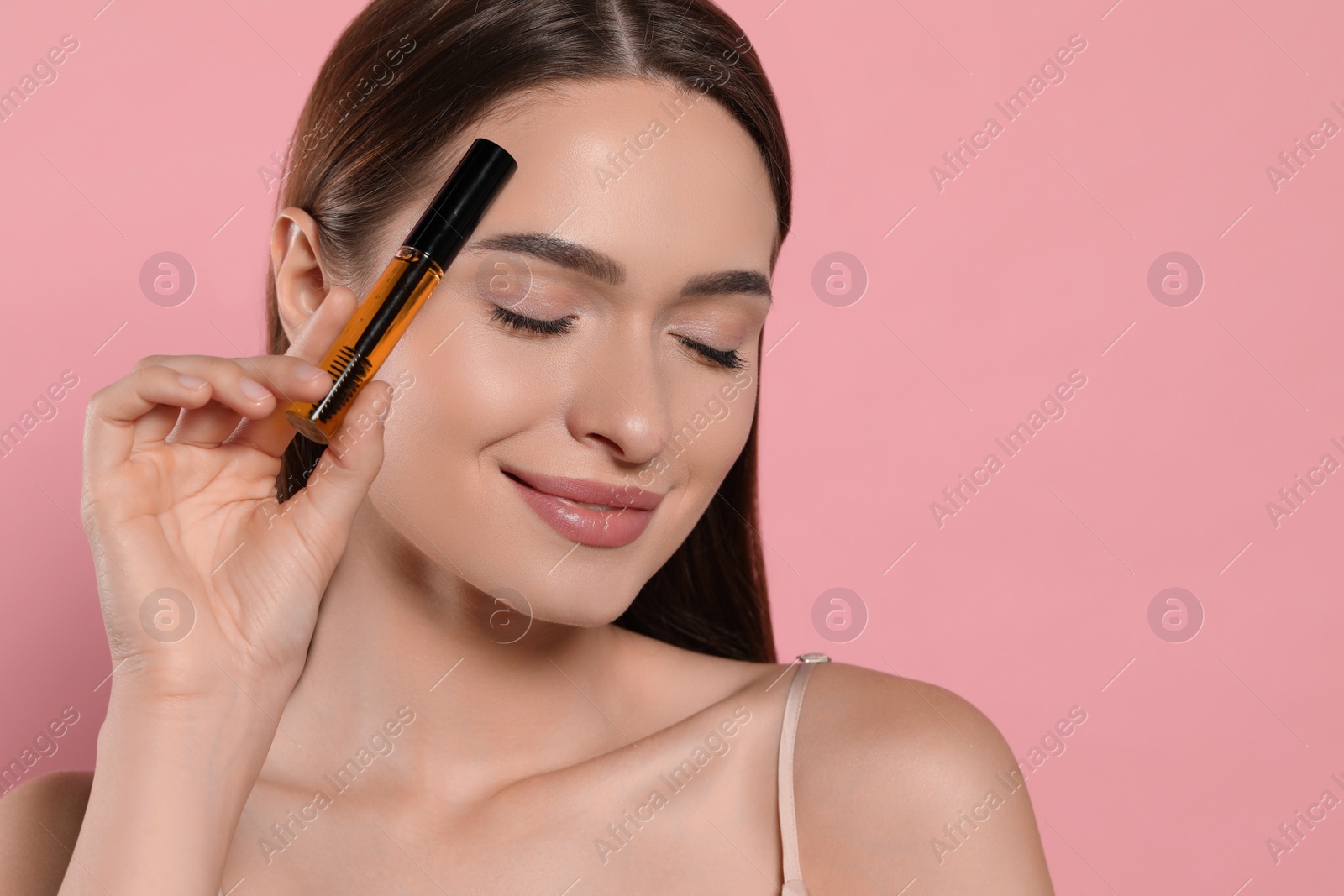 Photo of Young woman with eyelash oil on pink background, space for text