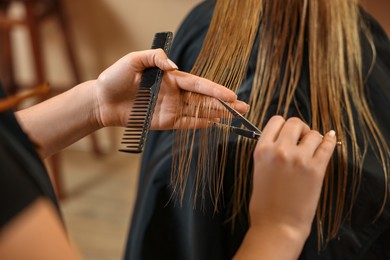Photo of Professional hairdresser cutting girl's hair in beauty salon, closeup