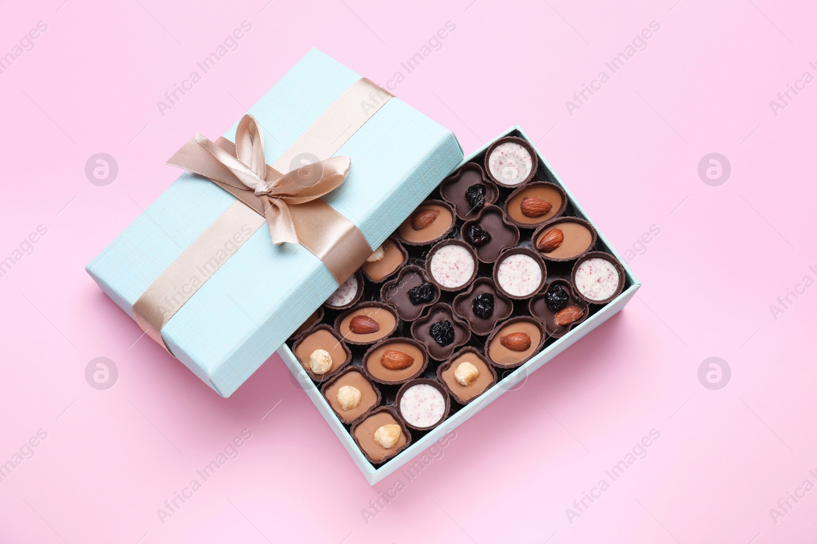 Photo of Open box of delicious chocolate candies on pink background, flat lay