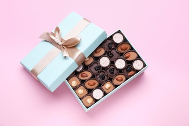 Open box of delicious chocolate candies on pink background, flat lay