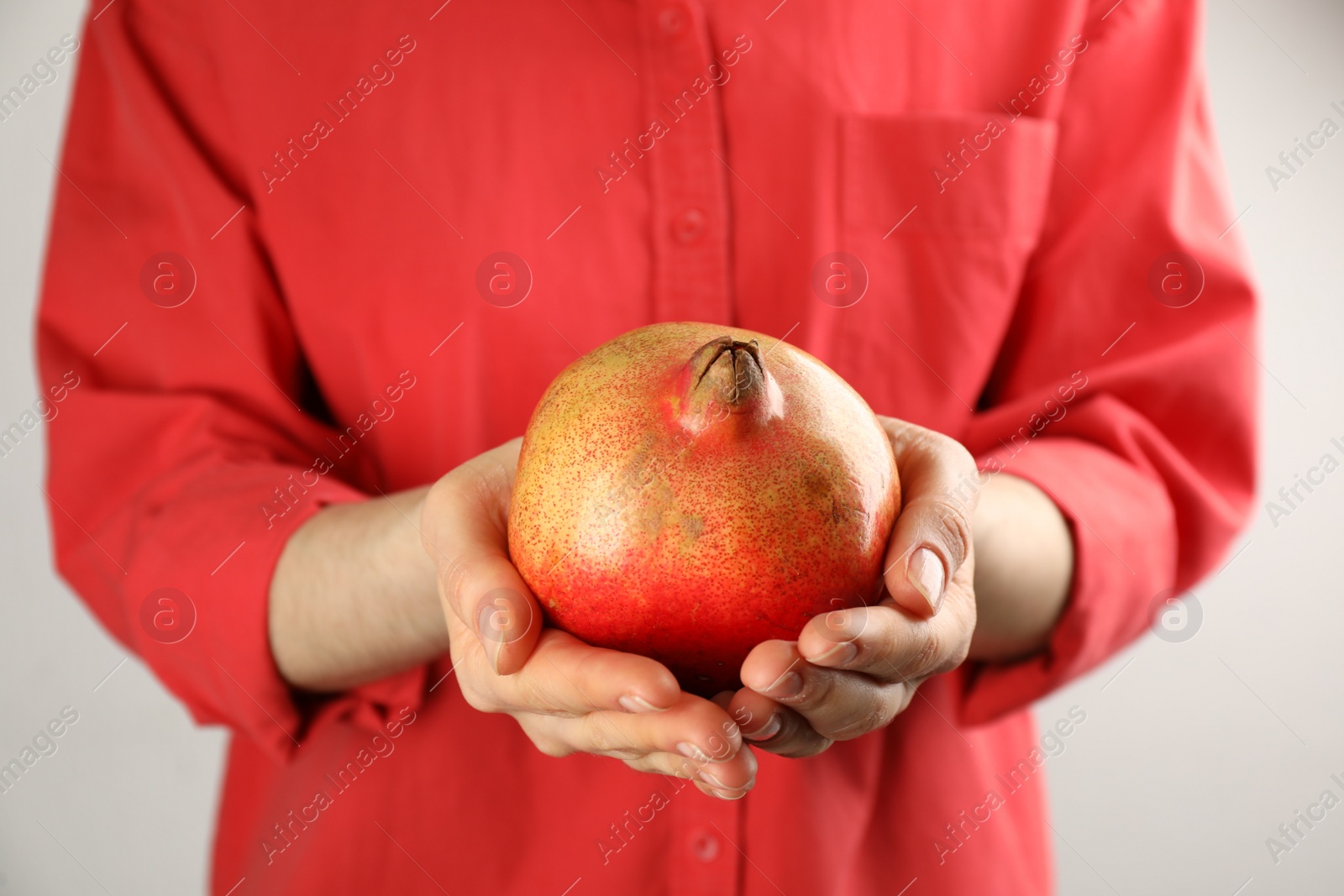 Photo of Woman holding ripe pomegranate on light background, closeup
