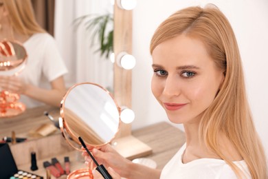 Photo of Beautiful woman applying makeup near mirror in room