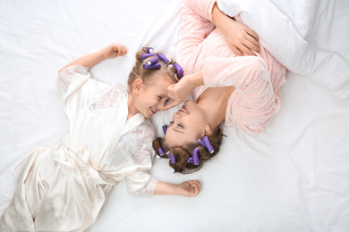 Photo of Happy mother and daughter with curlers lying on bed, top view