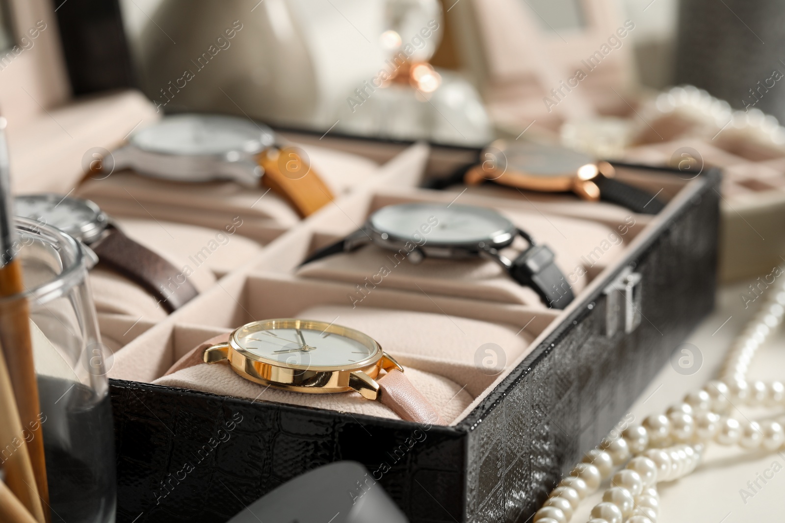 Photo of Jewelry box with many stylish wristwatches and pearl necklace on white table, closeup