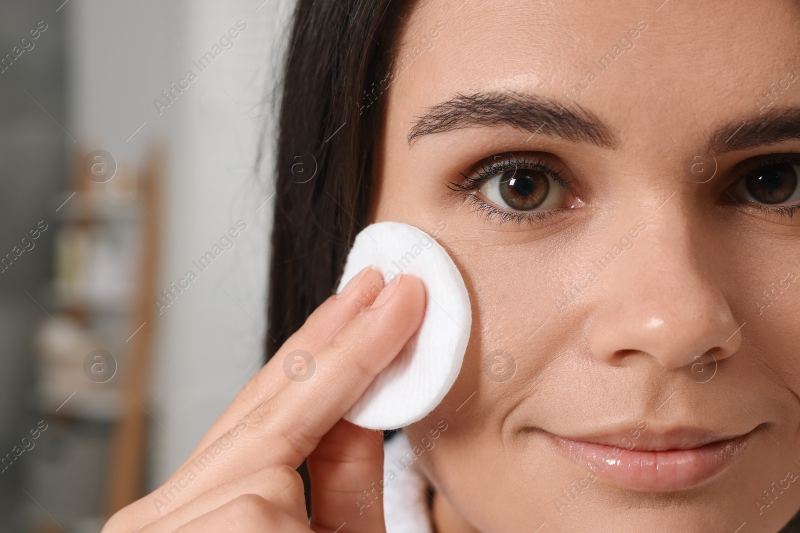 Photo of Young woman cleaning her face with cotton pad indoors, closeup