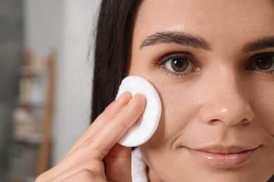 Photo of Young woman cleaning her face with cotton pad indoors, closeup