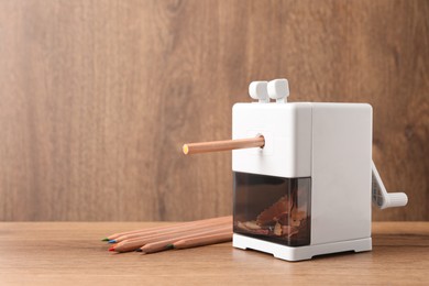 Mechanical sharpener near colorful pencils on wooden table. Space for text