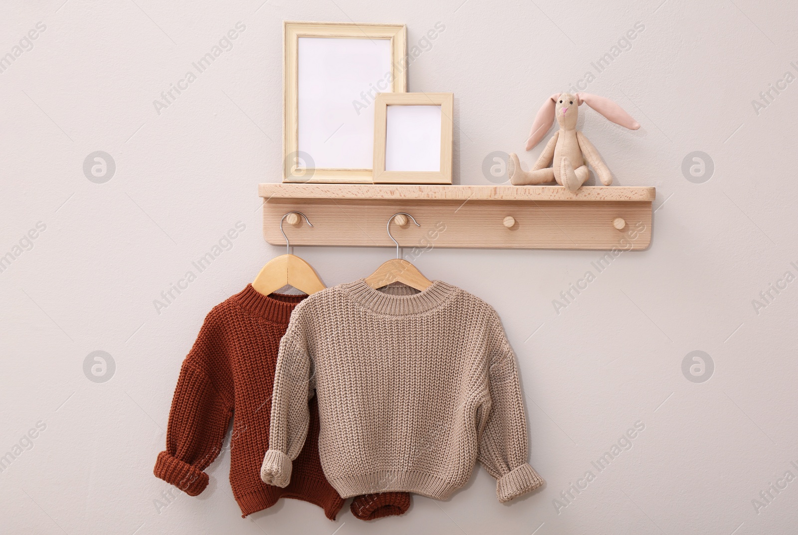 Photo of Wooden shelf with child's clothes, toy bunny and photo frames on beige wall. Interior element