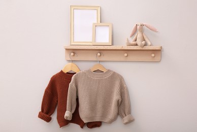 Photo of Wooden shelf with child's clothes, toy bunny and photo frames on beige wall. Interior element