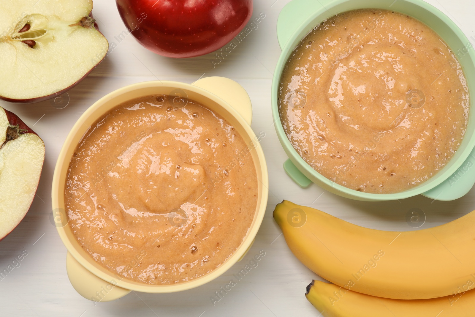 Photo of Bowls with puree and fruits on white wooden table, flat lay. Baby food