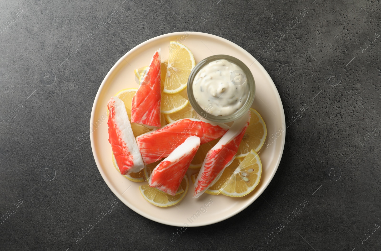 Photo of Delicious crab sticks with lemon slices and sauce on grey table, top view