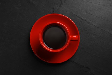 Photo of Red cup with aromatic coffee on black textured table, top view