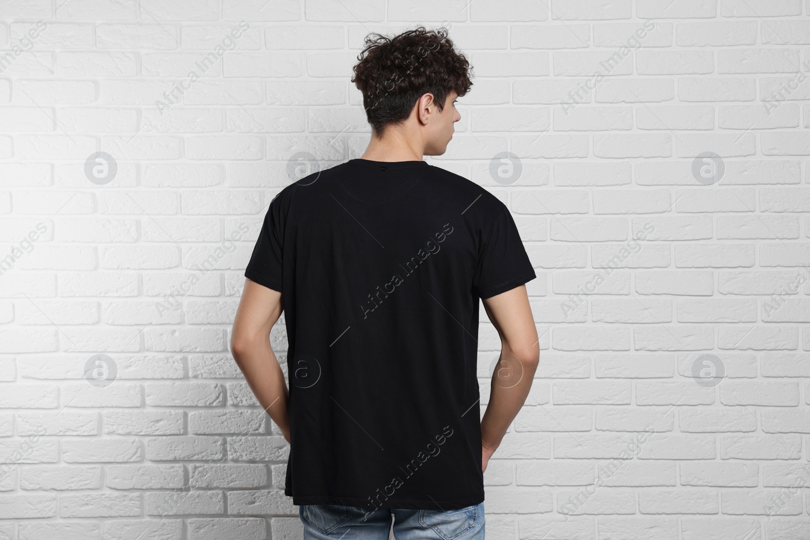 Photo of Man wearing black t-shirt near white brick wall, back view. Mockup for design
