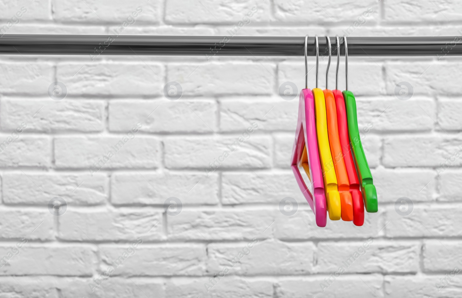 Photo of Clothes hangers on metal rail against brick wall background