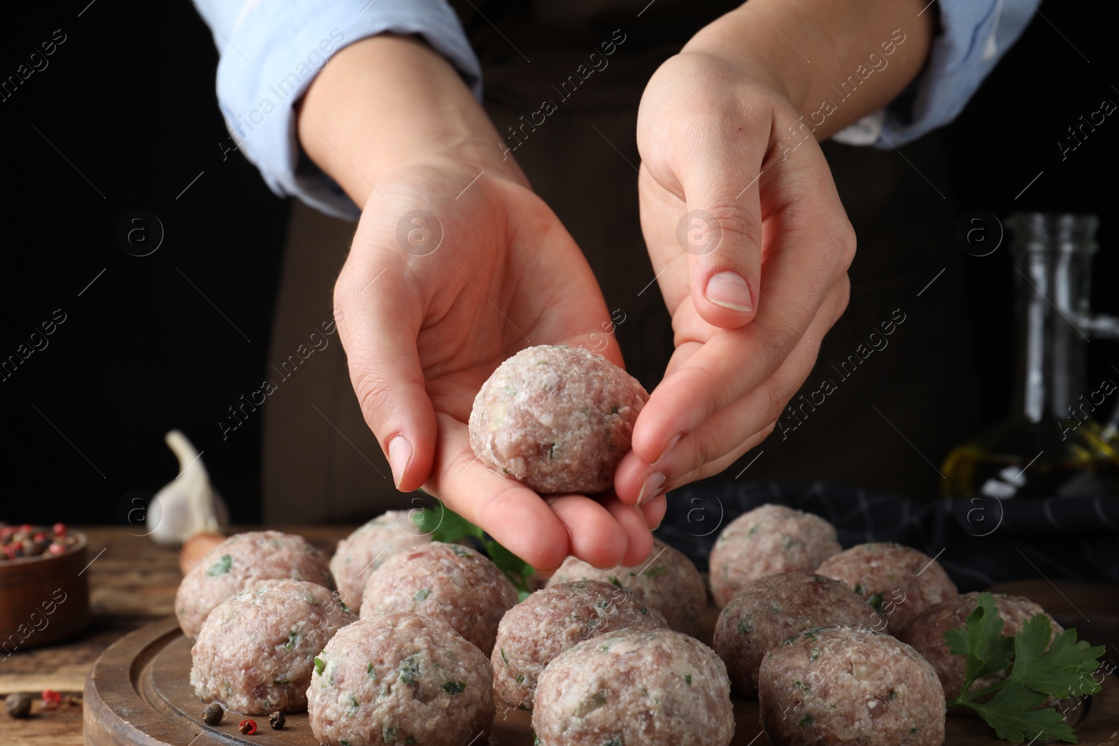 Photo of Woman making fresh raw meatballs at wooden table, closeup