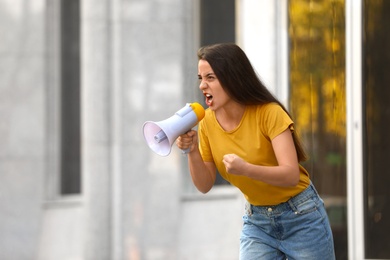 Image of Emotional young woman with megaphone outdoors. Protest leader