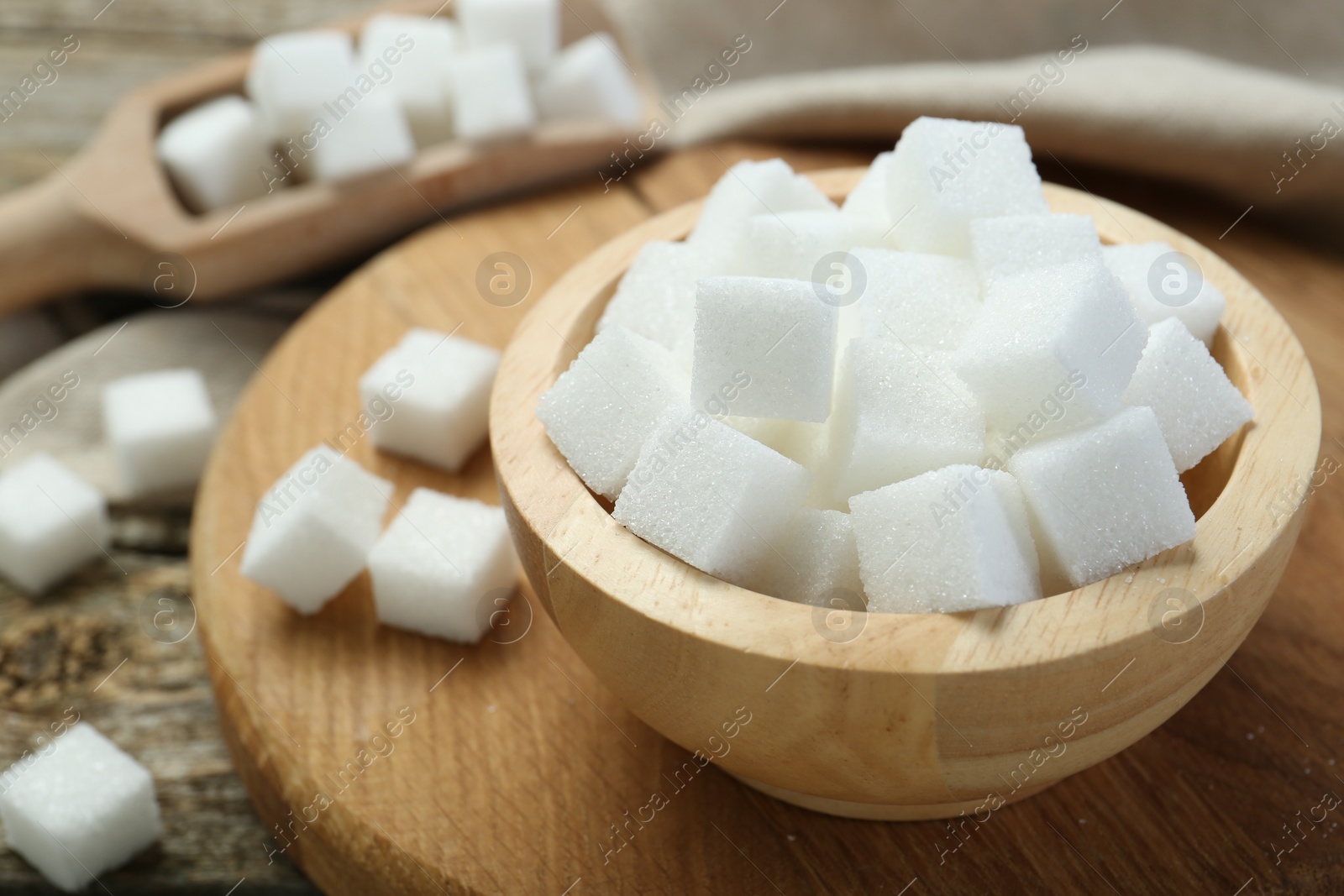 Photo of White sugar cubes in bowl and scoop on wooden table, closeup