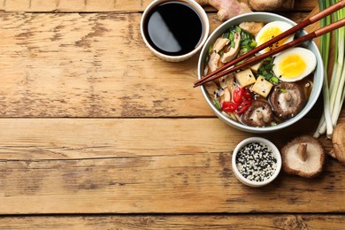 Photo of Bowl of delicious ramen and ingredients on wooden table, flat lay with space for text. Noodle soup