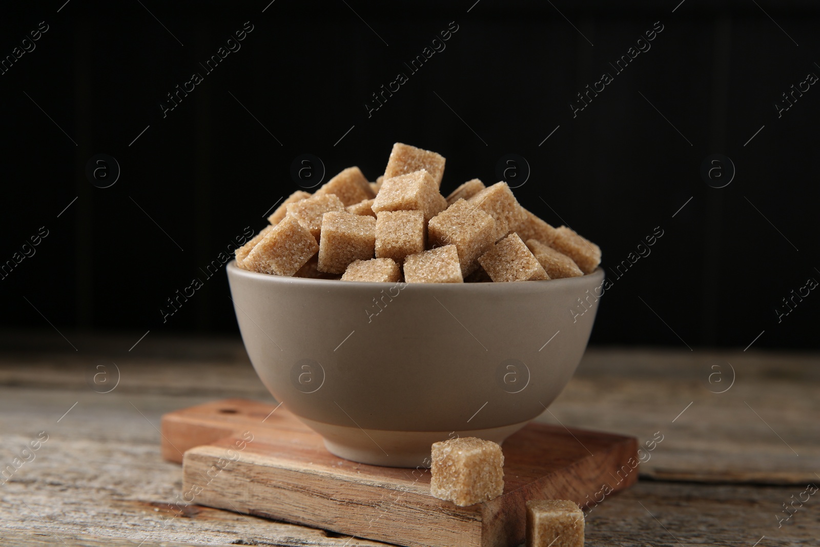 Photo of Brown sugar cubes in bowl on wooden table, closeup