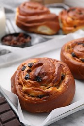 Delicious rolls with raisins and chocolate bar on white table, closeup. Sweet buns