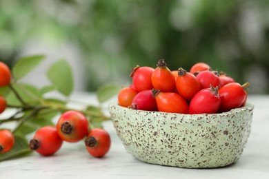 Photo of Ripe rose hip berries with green leaves on white wooden table outdoors, closeup. Space for text