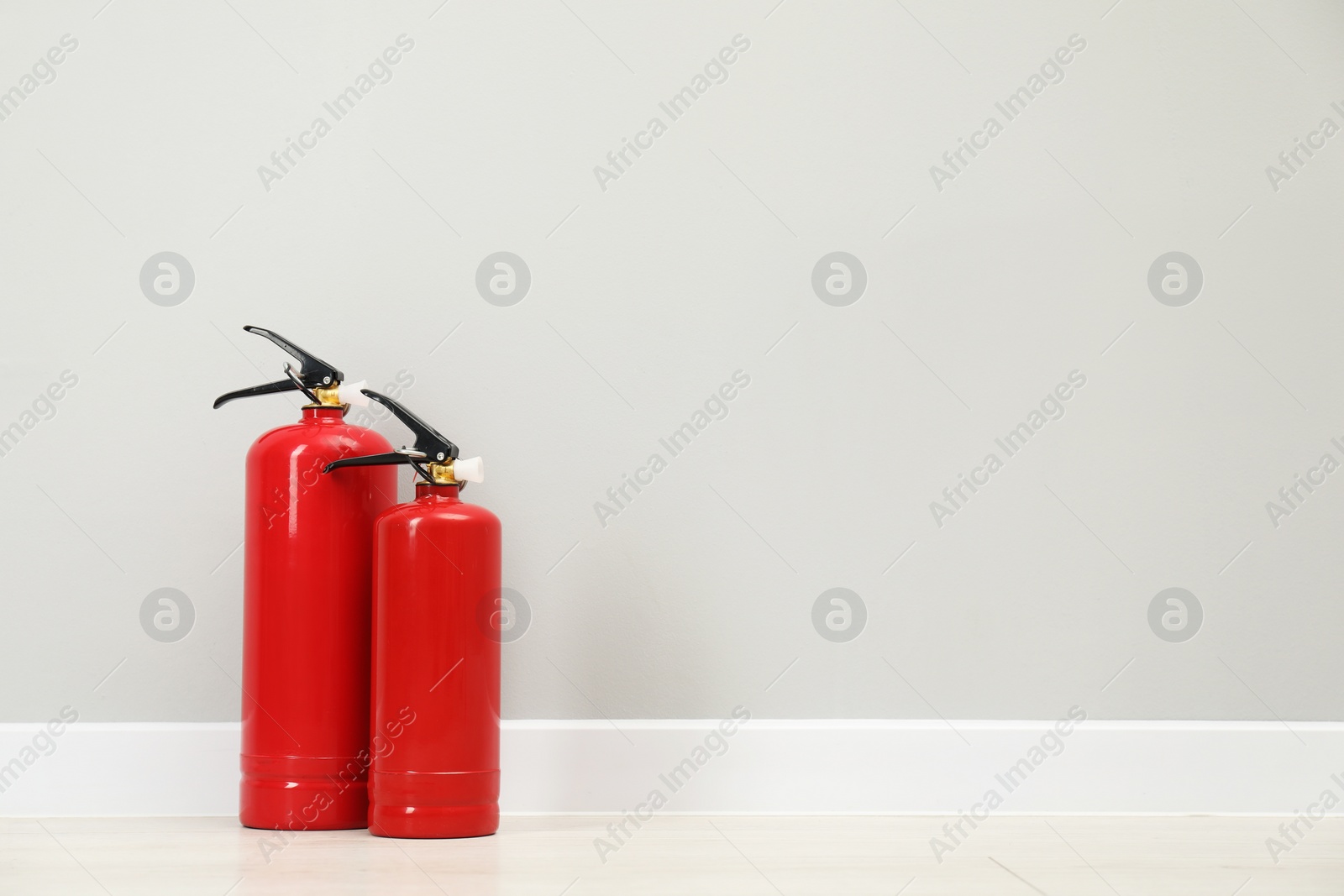 Photo of Fire extinguishers on floor near light grey wall, space for text