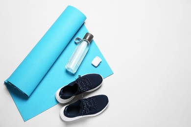 Photo of Exercise mat, bottle of water, wireless earphones and shoes on light grey background, flat lay. Space for text