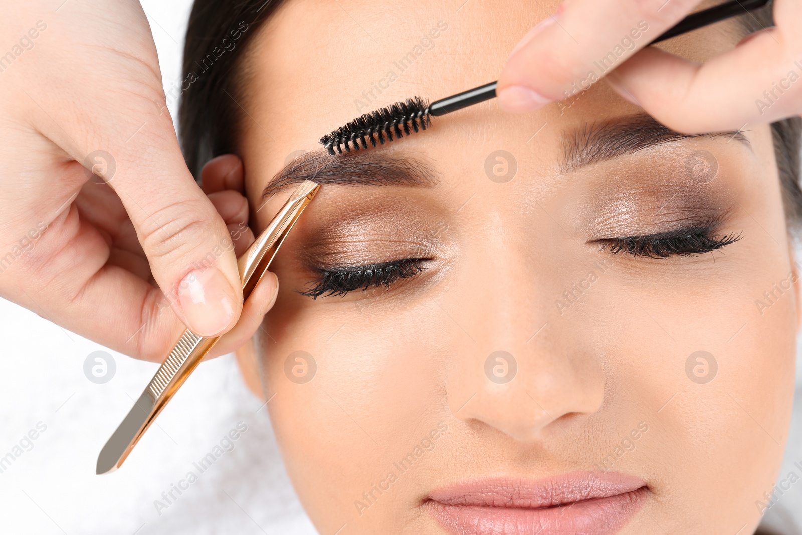 Photo of Young woman having professional eyebrow correction procedure in beauty salon