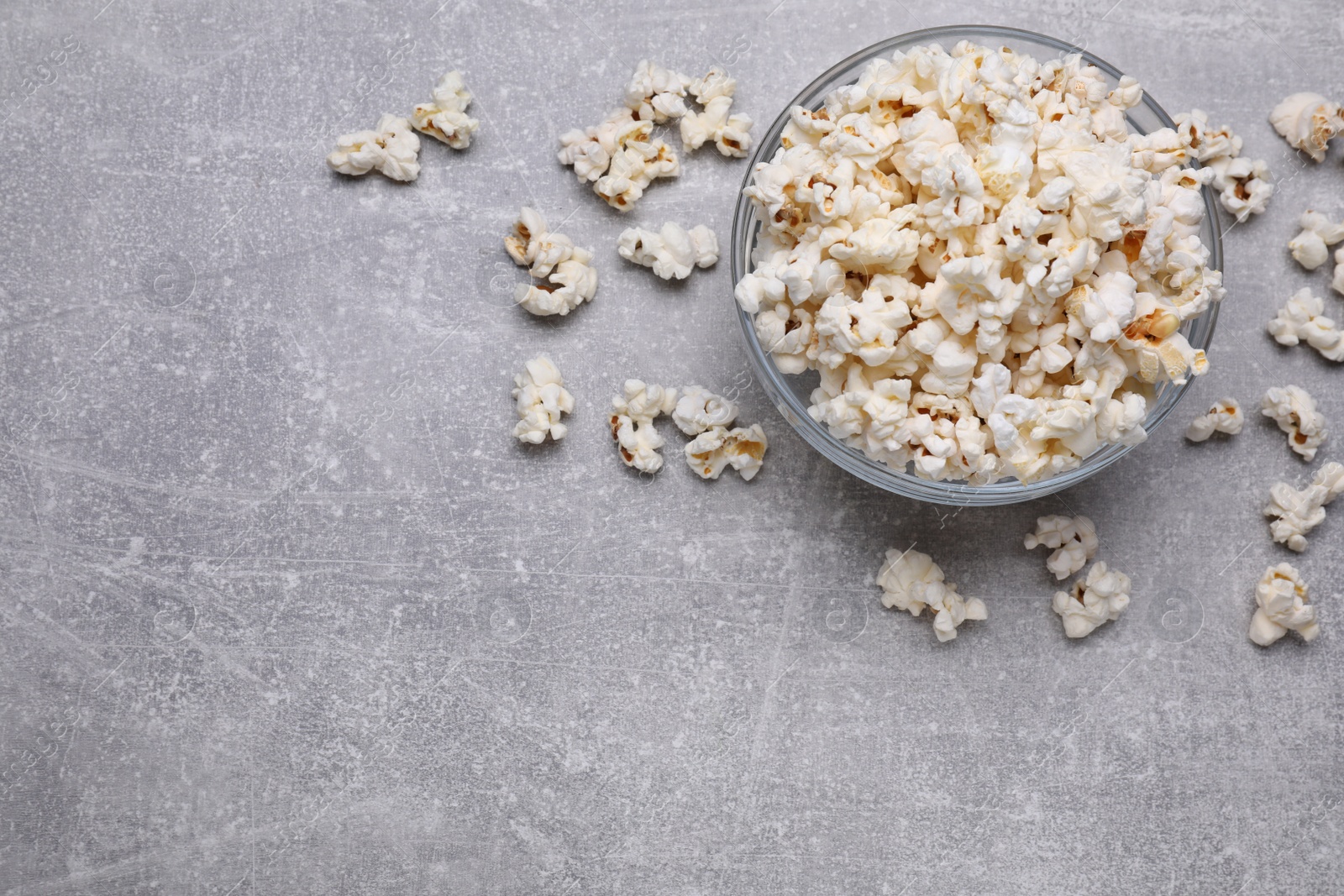 Photo of Bowl of tasty popcorn on grey table, flat lay. Space for text