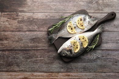 Fresh dorado fish, lemon slices and rosemary sprigs on wooden table, top view. Space for text