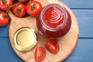 Photo of Organic ketchup in jar and fresh tomatoes on blue table, top view. Tomato sauce