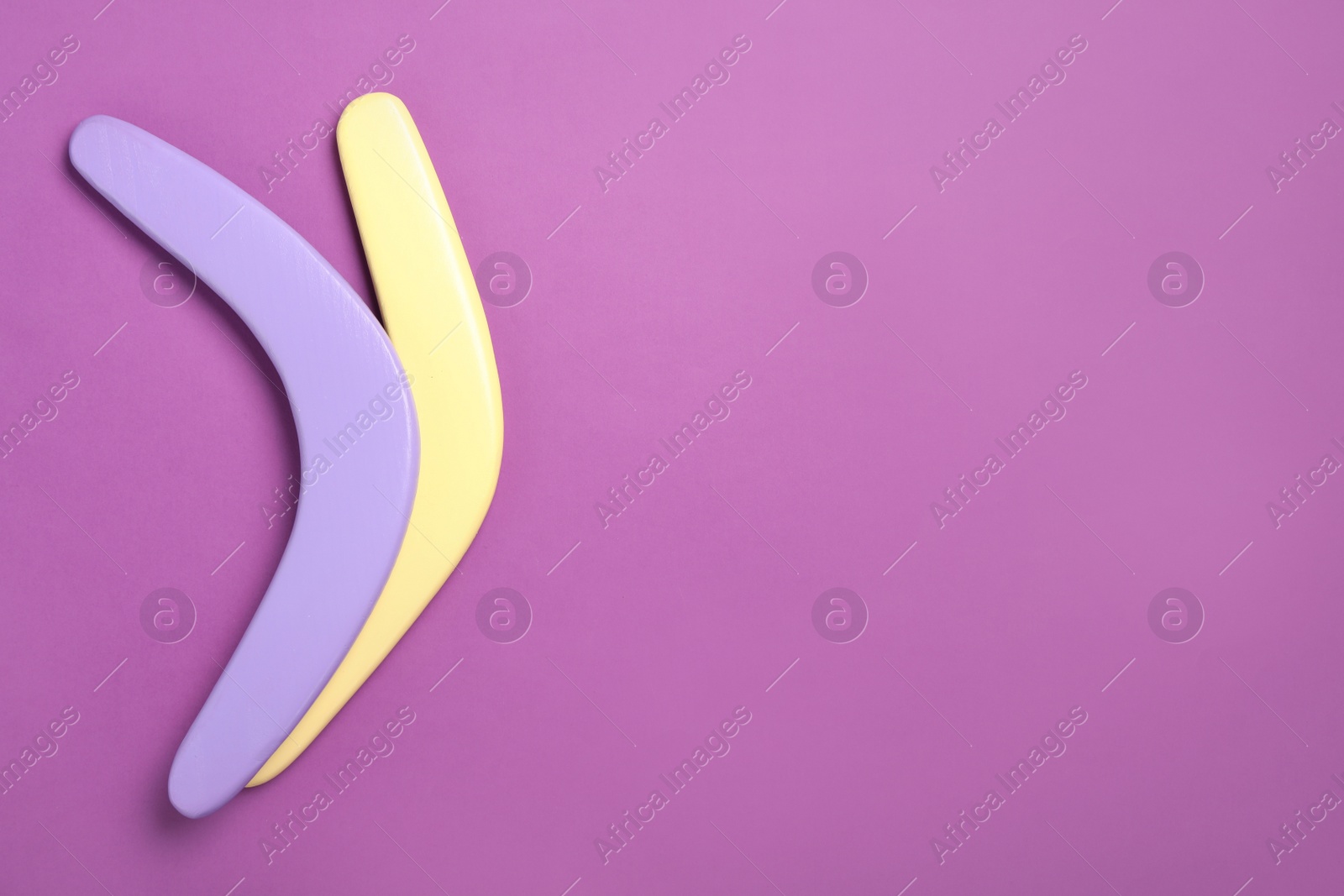 Photo of Colorful wooden boomerangs on purple background, flat lay. Space for text