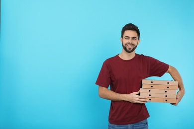 Photo of Young courier with pizza boxes on color background, space for text. Food delivery service