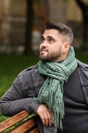 Photo of Smiling man in warm scarf on bench outdoors