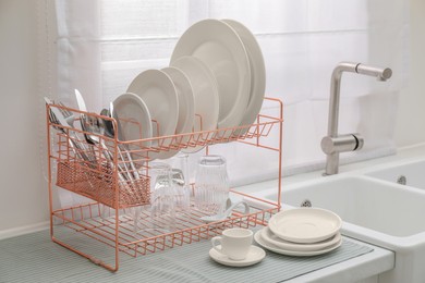 Photo of Drying rack with clean dishes on countertop near sink in kitchen