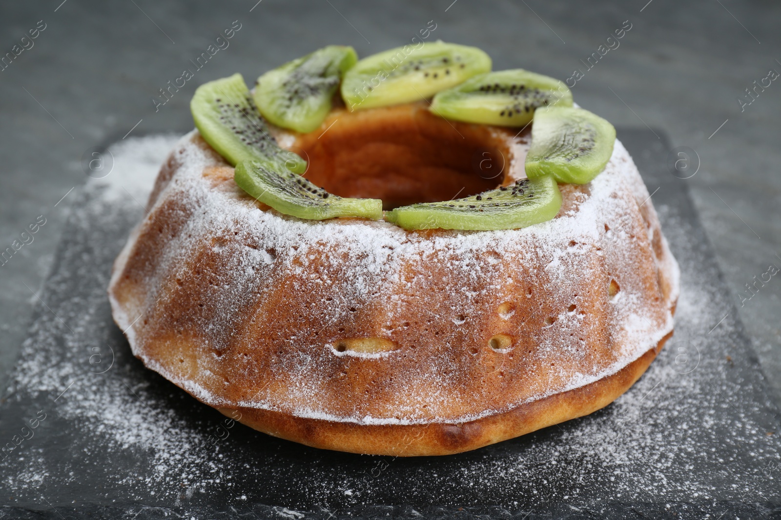 Photo of Homemade yogurt cake with kiwi and powdered sugar on black table