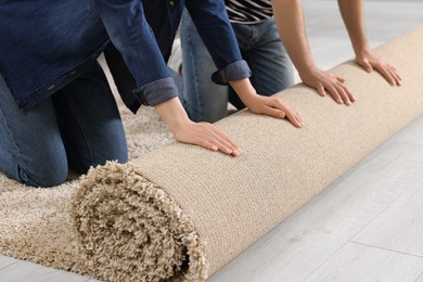 Photo of Couple unrolling new carpet in room, closeup