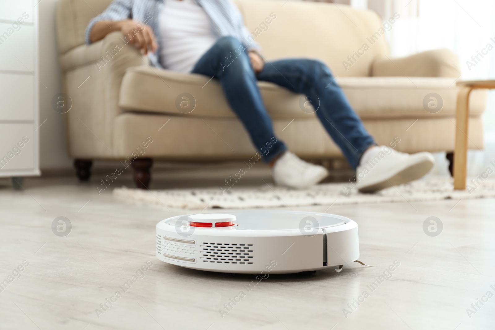 Photo of Man resting on sofa while robotic vacuum cleaner doing his work at home