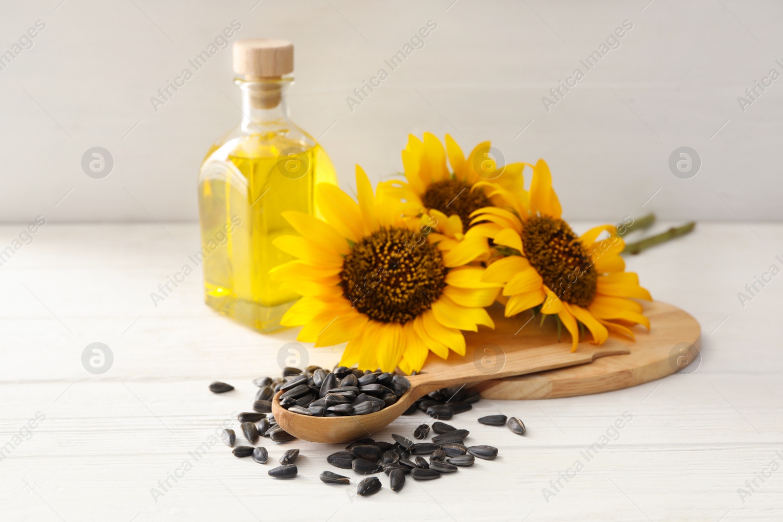 Photo of Sunflowers, bottle of oil and seeds on white wooden table