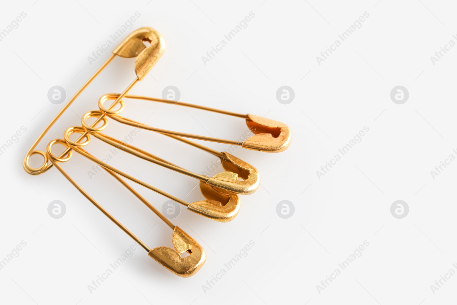 Photo of Golden safety pins on white background, closeup. Space for text