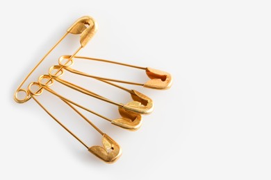 Photo of Golden safety pins on white background, closeup. Space for text