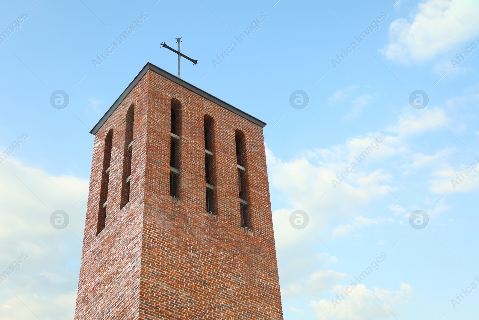 Photo of Beautiful brick church tower against blue sky, low angle view