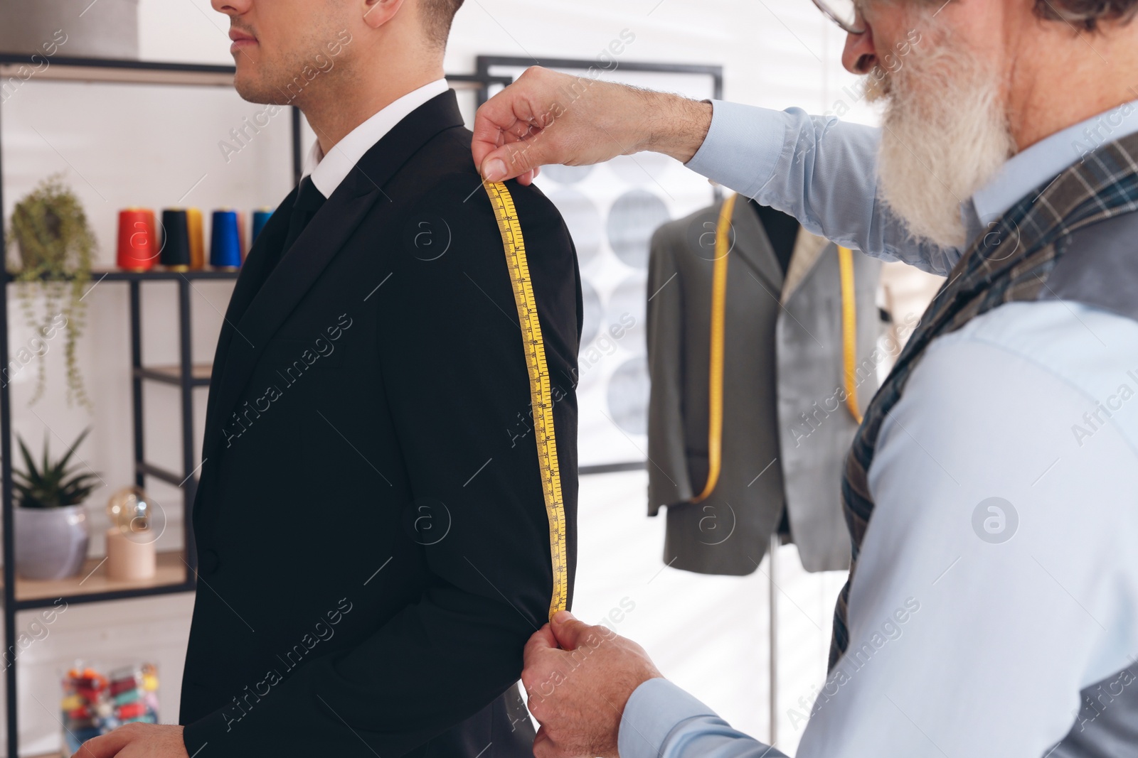 Photo of Professional tailor measuring jacket sleeve length in atelier, closeup