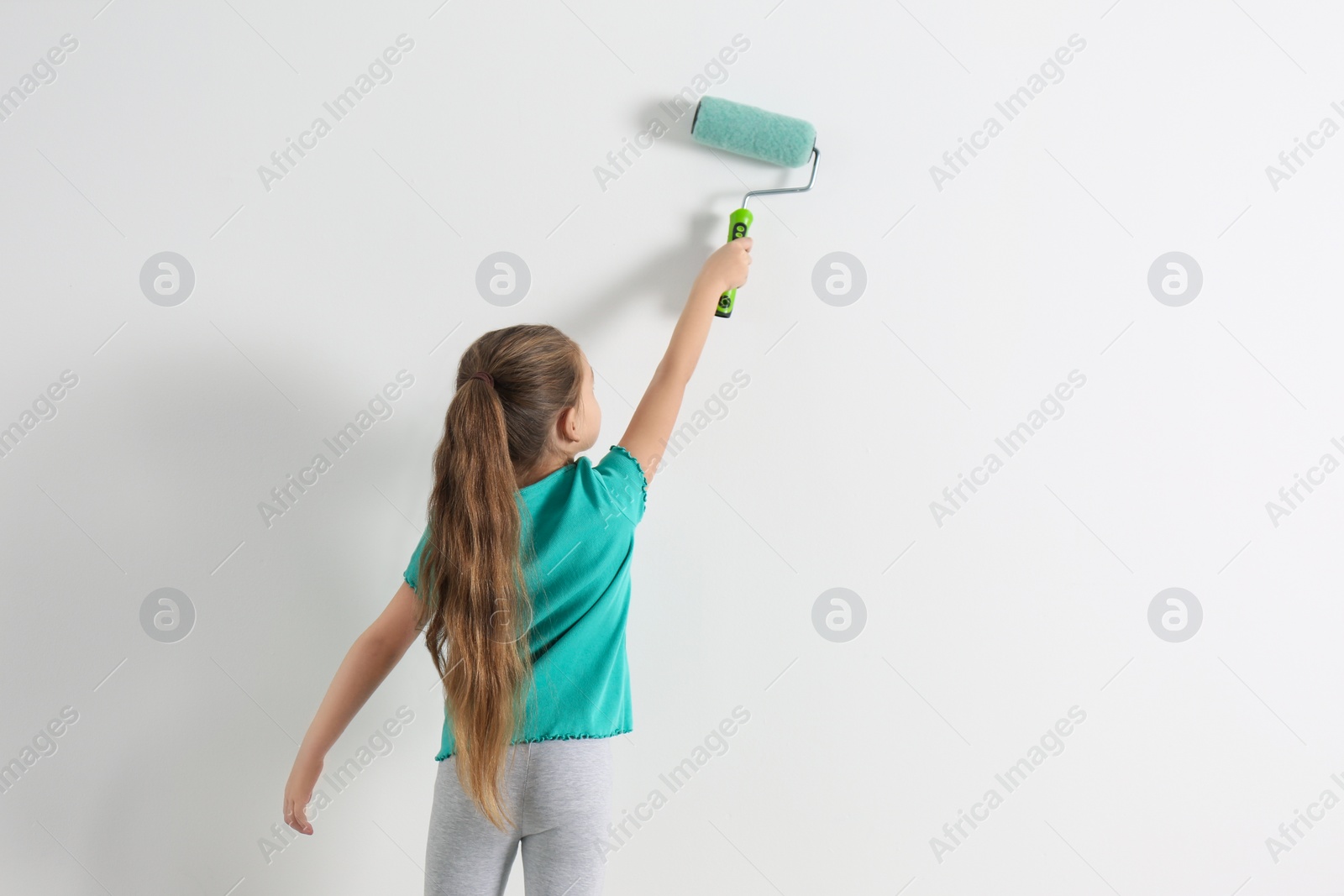 Photo of Little child painting with roller brush on white wall indoors. Space for text